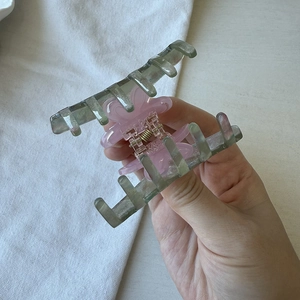 Close-up of a pink acetate flower hair claw clip with a green base and gold metal spring