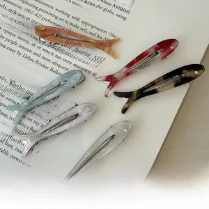 Close-up of six colorful fish-shaped acetate hair clips arranged on a vintage book