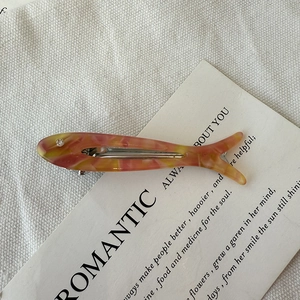 Macro detail of a fish-shaped acetate hair clip with pink and yellow marble patterns