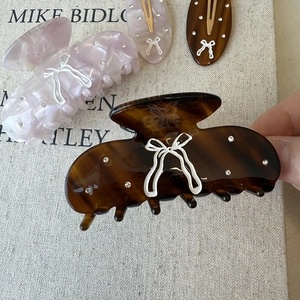 Elegant amber acetate bow hair claw clip with rhinestones on a rustic canvas background