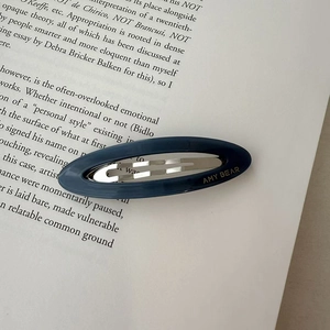 Detailed close-up of a blue oval acetate hair clip on a vintage book page backdrop