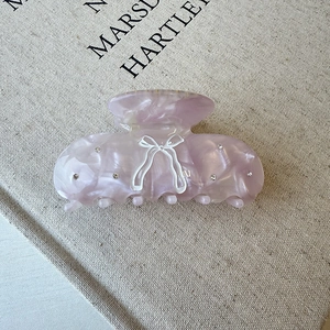 Detail of purple marble acetate hair claw with crystal bow design on a beige book