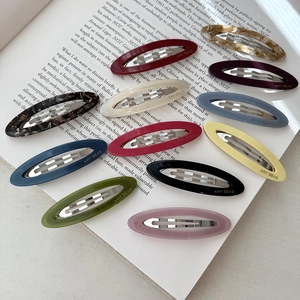 Set of 11 colorful acetate oval hair clips with metal snap closures on a book
