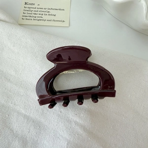 Close-up of a deep burgundy acetate hair claw clip with handmade lettering on fabric