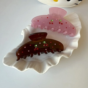 Sparkly rhinestone cherry hair claws in pink and brown acetate on a white ceramic tray