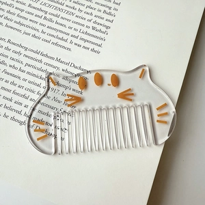 Macro detail of cute cat acrylic hair comb on book showing transparent material and teeth