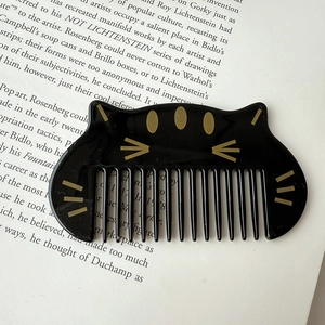 Portable cute black cat hair comb for kids, compact anti-static styling brush on a book