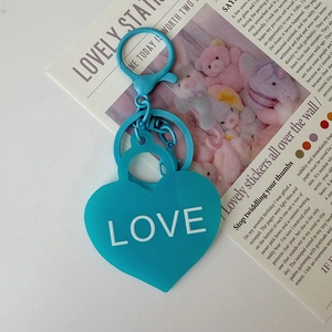 Détail du porte-clés coeur bleu sarcelle avec texte LOVE sur fond de journal