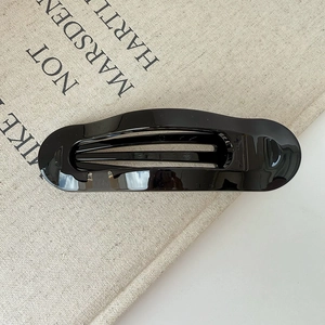 Vue détaillée d'une pince à cheveux ovale noire brillante sur un fond en lin minimaliste