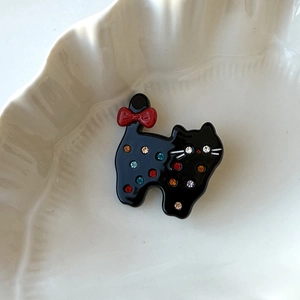Close-up of black cat hair clip featuring colorful rhinestones and a red bow accent