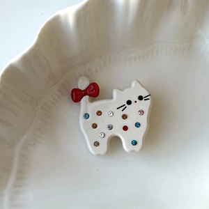 Macro detail of cat hair clip with colorful rhinestones and a red bow in a ceramic bowl