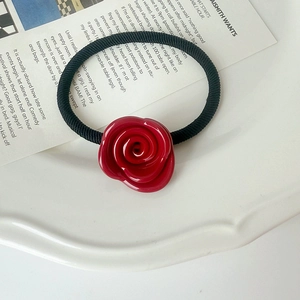 Detail view of a glossy red rose hair tie resting on an elegant white ceramic dish