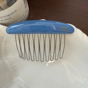 Detailed macro of a blue acetate hair comb with golden logo and silver metal teeth