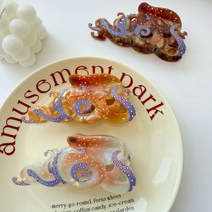 Three octopus acetate hair claws in brown, orange and pink on a beige ceramic plate