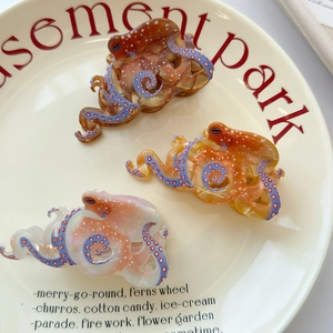 Three acetate octopus hair claws in tortoiseshell, orange, and pink on a ceramic tray