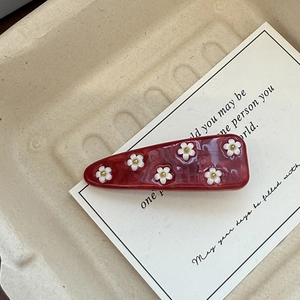 Detailed close-up of a red marble acetate hair clip with delicate white floral patterns