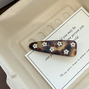 Detail of tortoise shell acetate hair clip with white flower motifs and gold beads