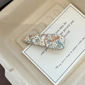 Detail of acetate hair clip with floral reliefs and marbled texture on card