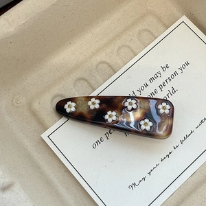 Detail of tortoiseshell acetate hair clip with white floral motifs and golden beads