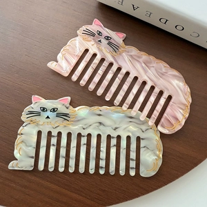 Cute cat-shaped acetate hair combs in pink and white marble finish on a wooden desk