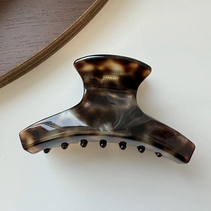 Detailed view of an amber-colored acetate hair claw clip on a clean white background