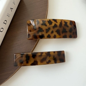 Detailed macro view of two leopard print acrylic spring hair clips on a minimalist background