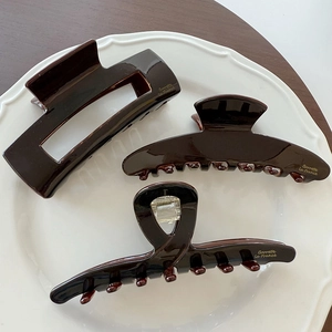 Three elegant chocolate brown French style hair claws displayed on a white ceramic plate