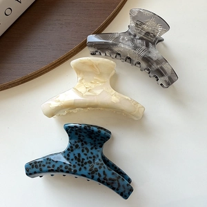 Three acetate hair claws in marble and leopard patterns on a wooden tray setting