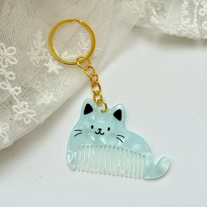 Close-up of mint green marble cat comb keychain with gold hardware on white lace