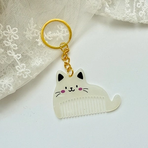 Detail view of a cat-shaped hair comb keychain in creamy white acrylic with gold ring