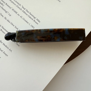 Close-up of tortoise shell pattern acetate hair clip on vintage book page with soft lighting