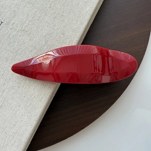 Close-up of a glossy red minimalist swallowtail hair clip on a textured book