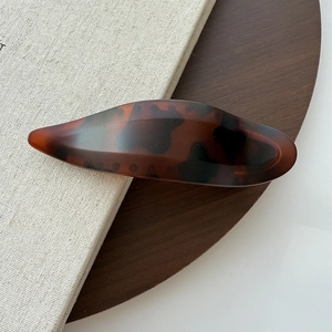 Detail of dark brown tortoiseshell hair clip in a sleek spindle design with acetate texture