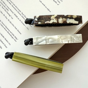 Three acetate hair clips in tortoiseshell, pearl white, and olive green on vintage book