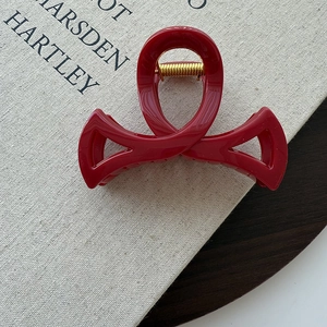 Détail d'une pince à cheveux nœud rouge foncé avec ressort doré posée sur un livre