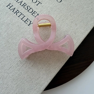 Gros plan détaillé d'une pince à cheveux rose translucide en forme de ruban sur un livre