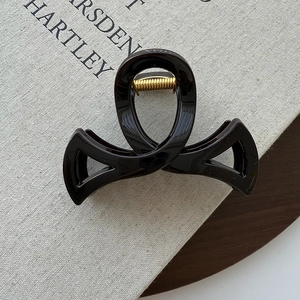Détail d'une pince à cheveux brillante avec design croisé et ressort doré sur un livre texturé
