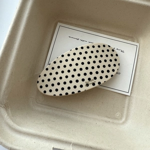 Close-up of oval acetic acid hair clip with black polka dots in minimalist packaging