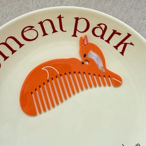 Detail view of a cute orange fox acetate hair comb displayed on a white ceramic plate
