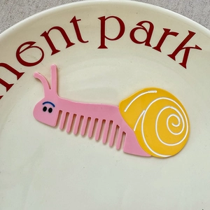 Detail of snail-shaped pink and yellow acetate pocket hair comb on a decorative plate