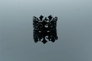 Macro shot of black gothic crown ring with fleur-de-lis and cross motifs on dark mirror