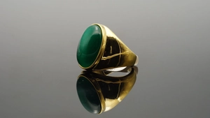 Dettaglio macro di una gemma verde ovale incastonata in un anello di acciaio al titanio dorato