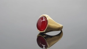 Detalle de anillo ancho dorado con una piedra preciosa roja de corte cabujón ovalado