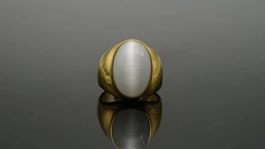 Macro di un anello ovale dorato con una grande pietra bianca a occhio di gatto