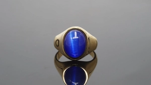 Detailopname van gouden roestvrijstalen ring met ovale blauwe kattenoogsteen op zwart