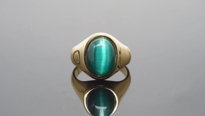 Close-up van een gouden roestvrijstalen ring met groene kattenoogsteen op een spiegel