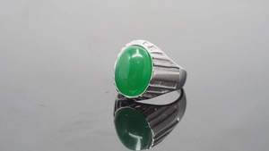 Makroaufnahme eines silbernen Titanrings mit großem grünen Stein und Rillenverzierung