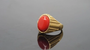 Makroaufnahme von vergoldetem Titanring mit rotem Edelstein und gestreifter Textur