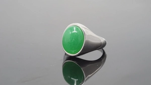 Primer plano de anillo de acero plateado con gema verde óvalo sobre superficie negra