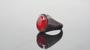 Detalle de anillo vintage de acero inoxidable con gema roja ovalada en fondo gris
